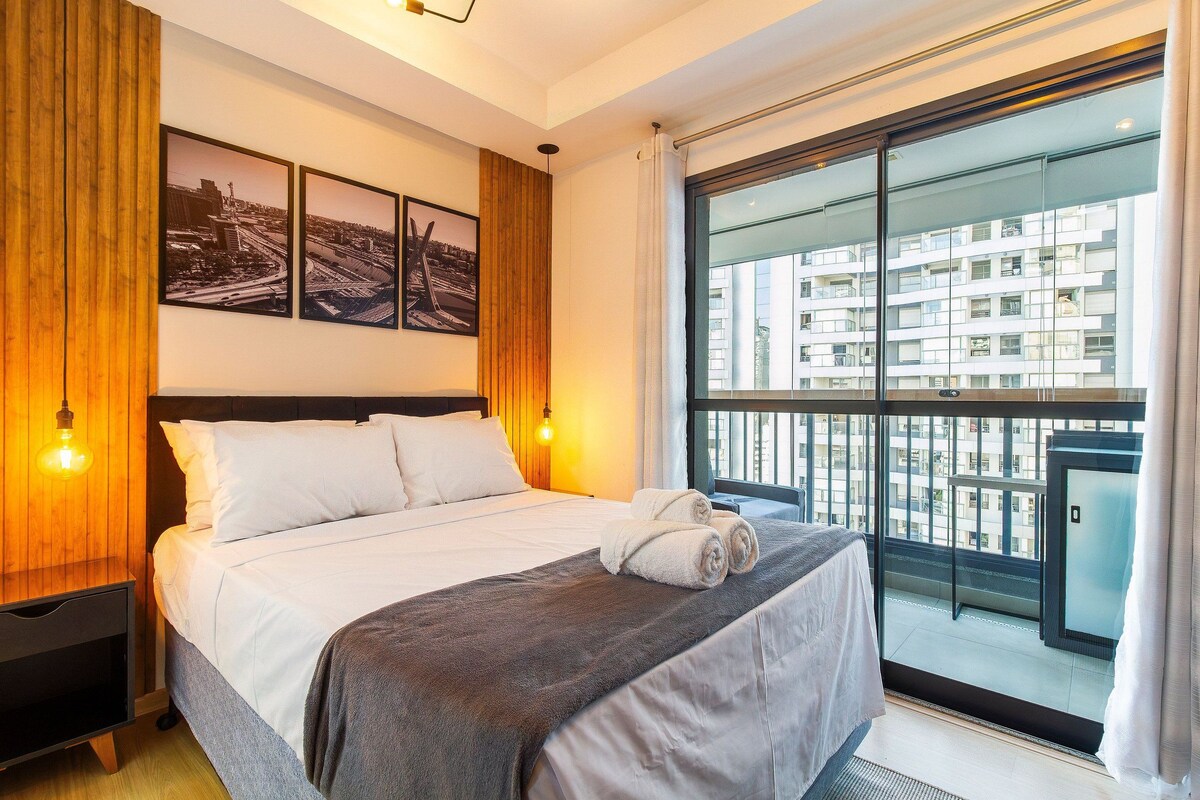 Une chambre d’hôtel avec un grand lit, une vue sur la ville par la fenêtre et un tableau encadré au mur.