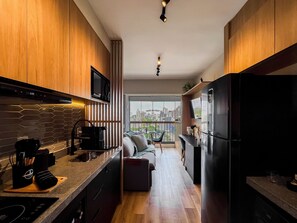 A modern kitchen with wooden cabinets, a built-in microwave, and a large refrigerator. - Innvista Uwin Brooklin (São Paulo)