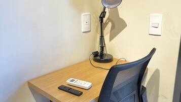 A corner desk with a chair, a desk lamp, a remote control, and a power strip.