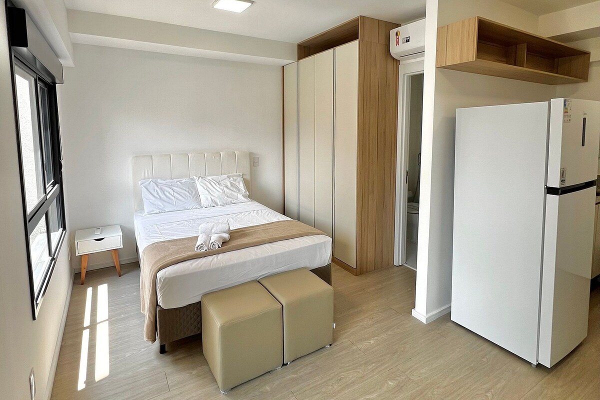 Une chambre à coucher comprenant un lit, des tables de chevet, un banc, une armoire et un réfrigérateur blanc.