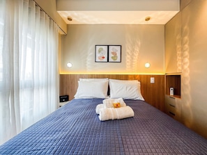 Quarto de hotel com cama, mesa de cabeceira, telefone fixado na parede e janela com cortinas.