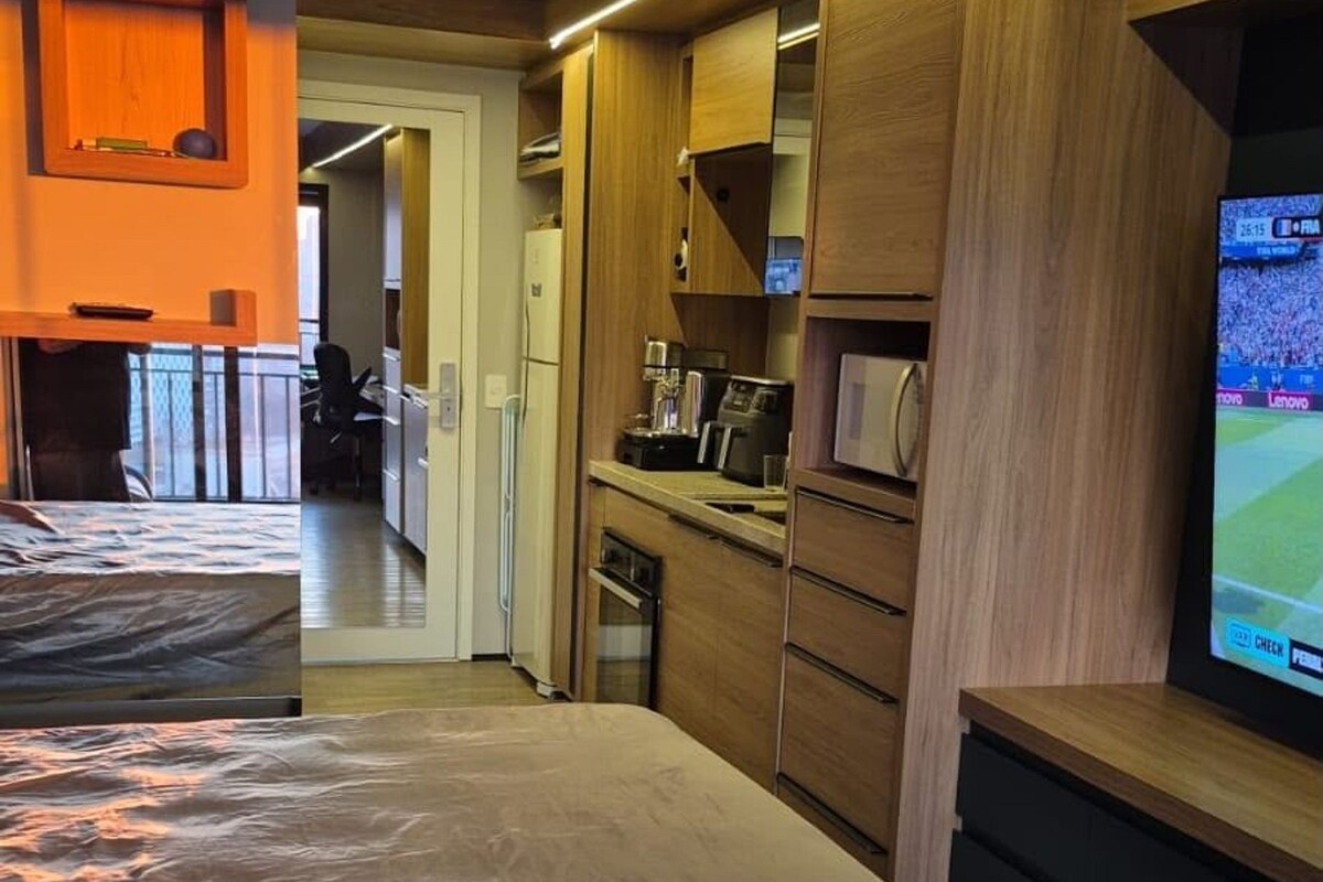 Een moderne hotelkamer met een groot bed, een kitchenette, een televisie en uitzicht op de gang.