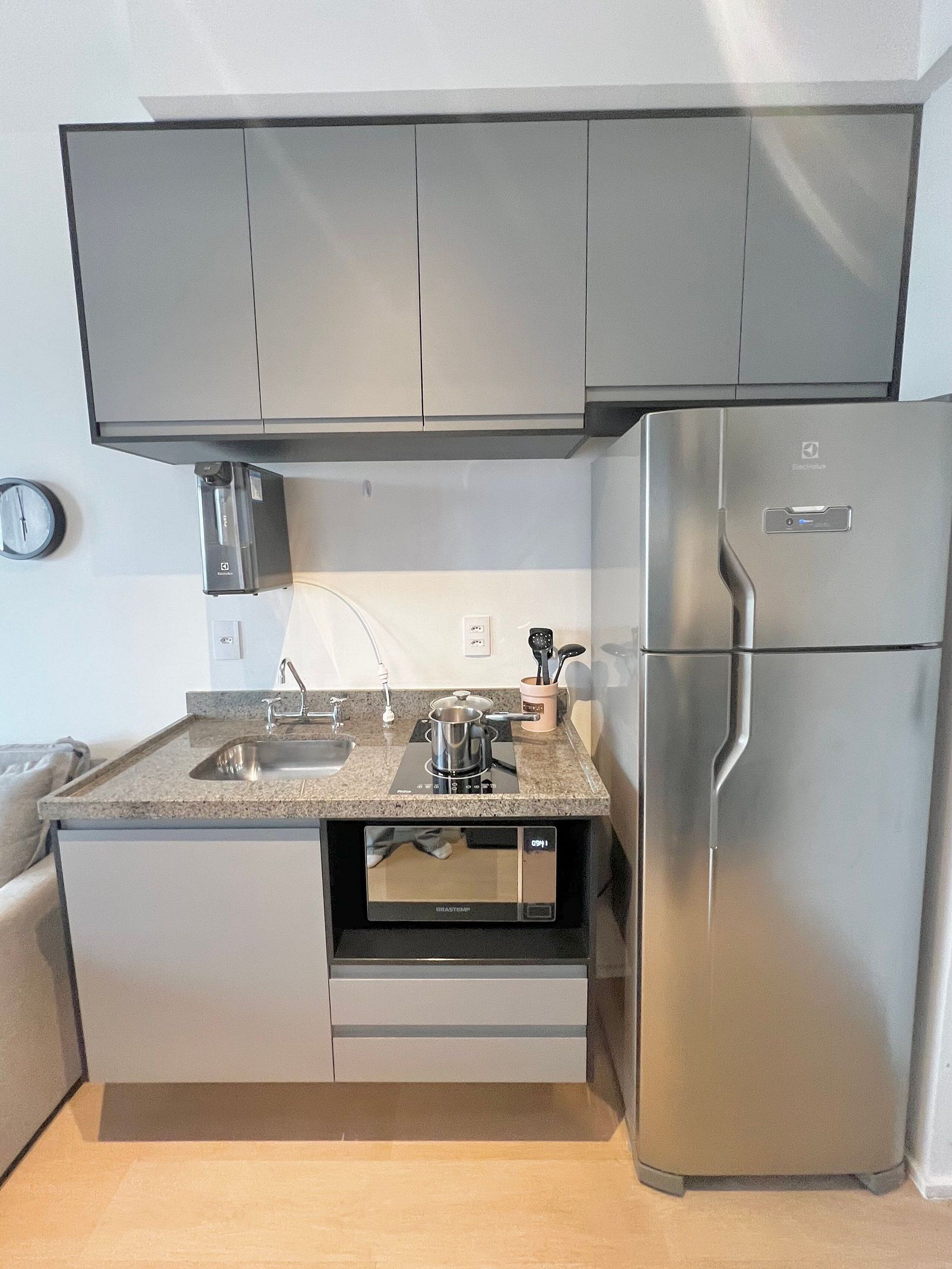 Uma cozinha compacta com micro-ondas integrado, geladeira de aço inoxidável e bancada de granito.