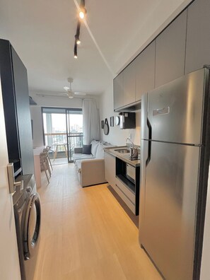 A modern kitchen with a built-in oven, a large refrigerator, and a dining area with a sofa and chairs. - Innvista Uwin Brooklin (São Paulo)