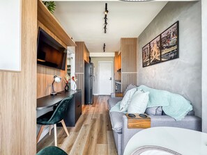 A modern kitchen with a built-in fridge, a dining area with a table and chairs, and a living area with a sofa and a TV. - Innvista Uwin Brooklin (São Paulo)