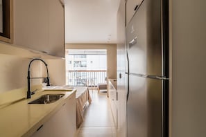 A narrow kitchen with a sink, a refrigerator, and a dining area with a table and chairs.