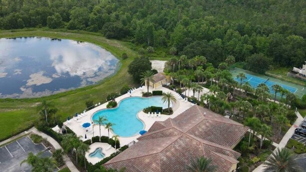 An aerial view of a resort with a large swimming pool, tennis courts, and a natural lake. - Cozy condo 10 min from Disney (Kissimmee)