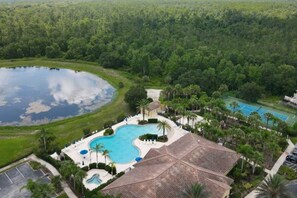 An aerial view of a resort with a large swimming pool, tennis courts, and a natural lake.