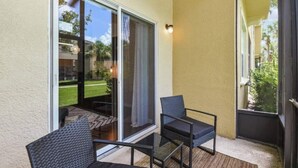 A balcony with two chairs, a glass table, and a sliding glass door leading to a patio. - Cozy condo 10 min from Disney (Kissimmee)