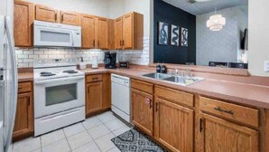 A modern kitchen with wooden cabinets, a white stove, a microwave, and a dishwasher. - Cozy condo 10 min from Disney (Kissimmee)