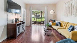 A spacious living room with a flat-screen TV, a sofa, a coffee table, and a ceiling fan. - Cozy condo 10 min from Disney (Kissimmee)