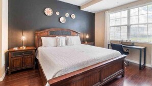 A bedroom with a large bed, a desk, and a window with blinds. - Cozy condo 10 min from Disney (Kissimmee)