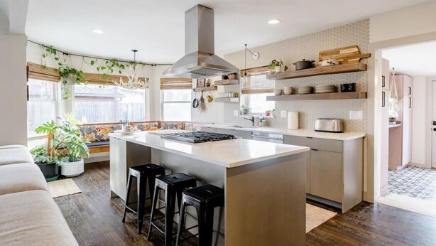 Una cocina moderna con una isla central, taburetes de bar, plantas colgantes y estantes empotrados.