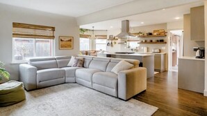 Una sala moderna con un sofá modular, una mesita redonda y un ventanal con persianas.