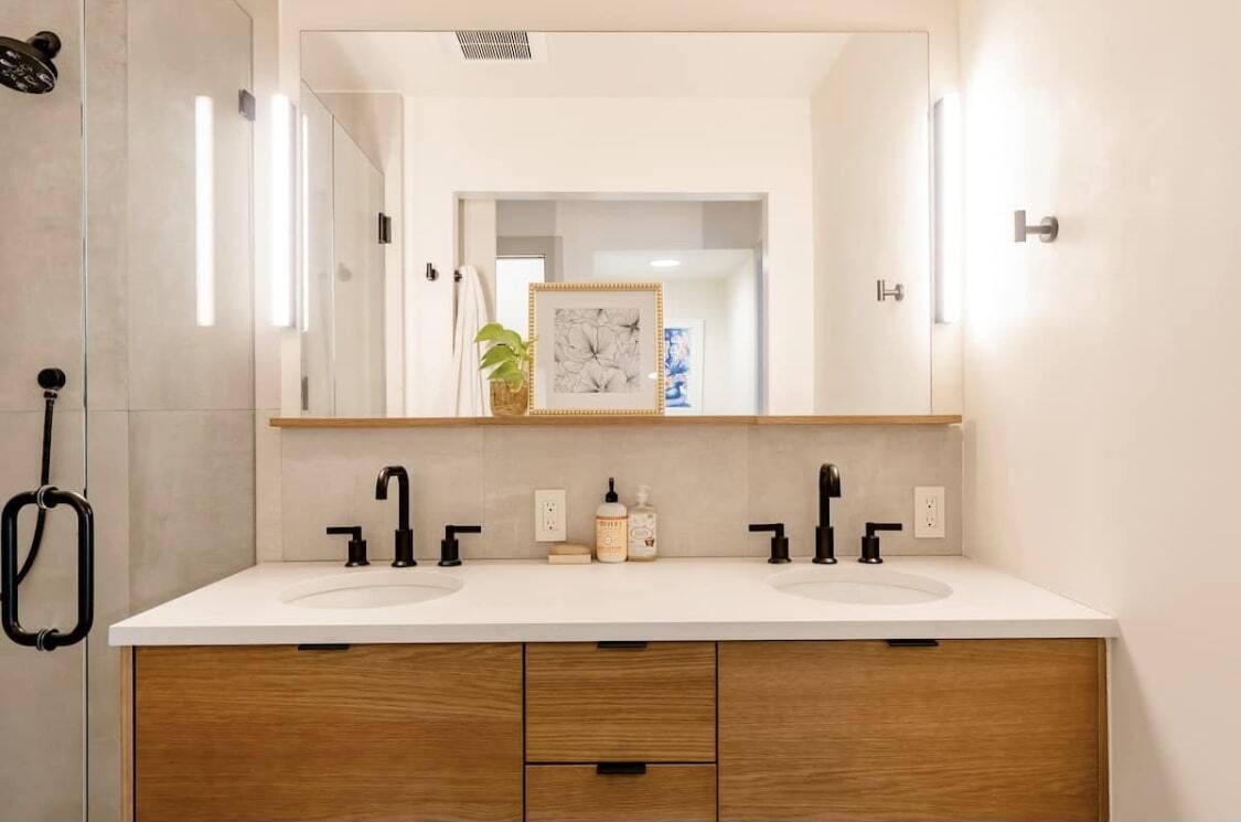 A modern bathroom with two sinks, wooden cabinets, and a large mirror.