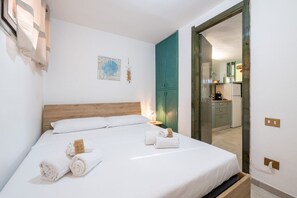 A neatly made bed with rolled towels, a wooden headboard, a teal cabinet, and a small wall decoration. - Villa Matilde Dream Oasis (Villasimius)