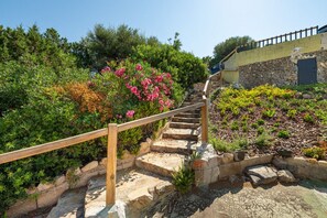 Un escalier en pierre avec une rampe en bois mène à un bâtiment dont le mur est en pierre et la porte est bleue.