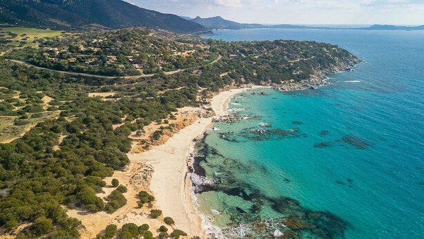 An aerial view of a coastal area with a beach, clear turquoise waters, and a mountainous backdrop. - Villa Matilde Dream Oasis (Villasimius)