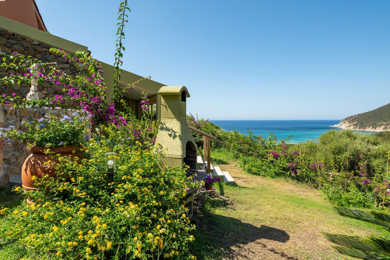 Une propriété située sur la côte, dotée d’une façade en pierre, d’un petit jardin agrémenté de fleurs jaunes et offrant une vue sur la mer.