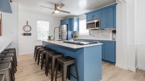 Una cucina moderna con mobili blu, un'isola centrale con sgabelli, elettrodomestici in acciaio inossidabile e una ventola a soffitto.
