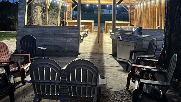 Una baita di legno rustica con un portico coperto, arredata con poltrone Adirondack e un barbecue.