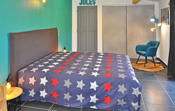 A bedroom with a bed, a chair, a door labeled "JULES", and a lamp.