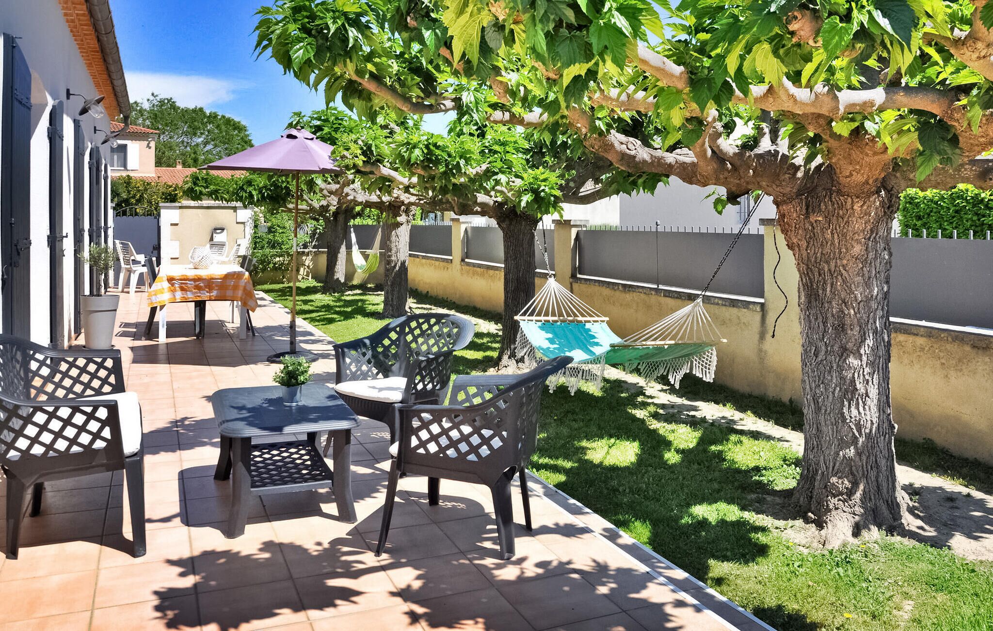 Un patio exterior con una mesa, sillas, una hamaca y un árbol que da sombra.