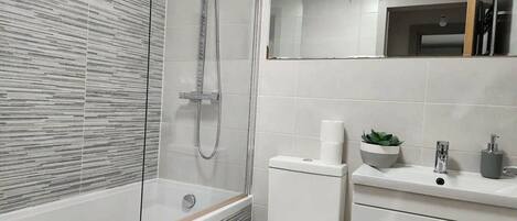 A modern bathroom with a glass-enclosed shower, a white toilet, and a vanity with a mirror and sink.