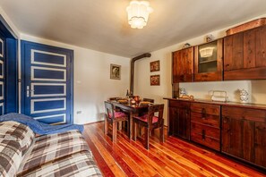 A room with a bed, a dining table with chairs, wooden cabinets, and a ceiling light fixture.