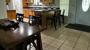 A kitchen with wooden cabinets, a dining table with chairs, a refrigerator, and a window with blinds.