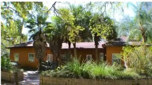 A single-story house with a red roof, surrounded by a variety of trees and shrubs.