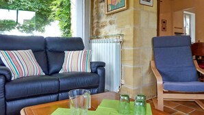 A living room with a black leather sofa, a blue armchair, and a wooden coffee table with green placemats and clear glasses. - Beautiful home in Domme with WiFi (Domme)
