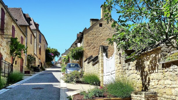 A narrow street lined with stone buildings, a car parked on the side, and a gate in the foreground. - Beautiful home in Domme with WiFi (Domme)
