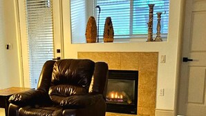 Un salon avec un canapé en cuir, une cheminée et une fenêtre agrémentée d’objets décoratifs.