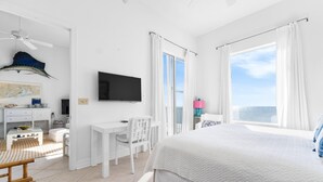 A bedroom with a large bed, a desk, a chair, a television, and a view of the ocean. - Spanish Key 703 (Pensacola)