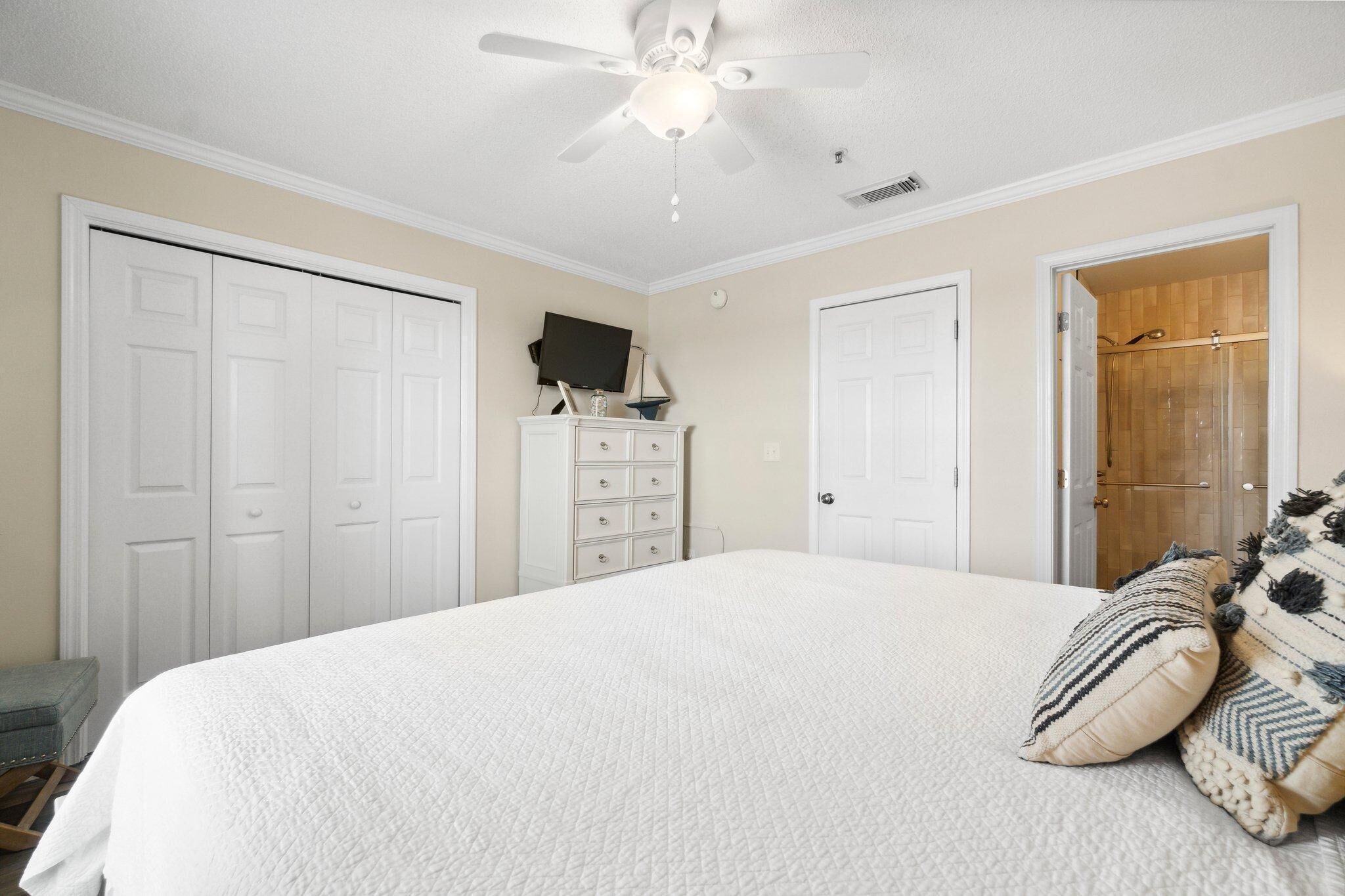 A bedroom with a large bed, a ceiling fan, a dresser, and a walk-in closet.