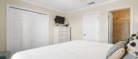 A bedroom with a large bed, a ceiling fan, a dresser, and a walk-in closet.