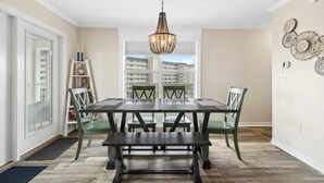 A dining area with a dark wooden table and green chairs, a chandelier, and a view of buildings through a large window. - Grand Caribbean East 417 (Pensacola)