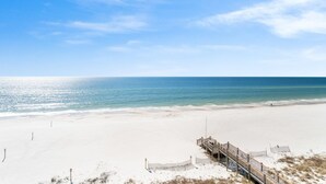 A beach with a wooden walkway leading to a pier, white sand, and clear blue water. - Windemere 502 (Pensacola)