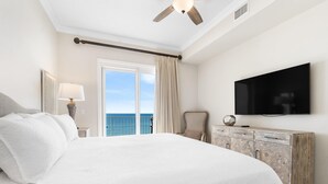 A hotel room with a large bed, a television, a wooden dresser, and a balcony with a view of the ocean. - Windemere 502 (Pensacola)