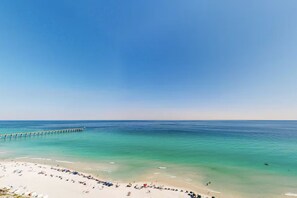 A beach with a pier extending into the water, a sandy shore with beach umbrellas, and a clear blue sky. - Sundunes 111 (Navarre)