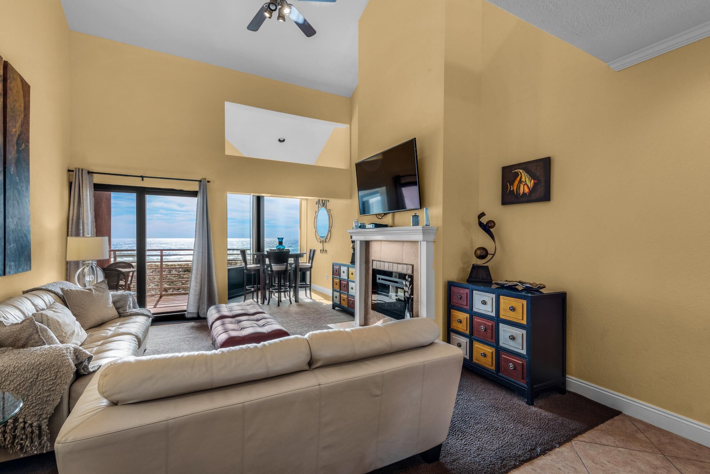A living room with a beige sofa, a fireplace, a TV, and a view of the ocean.