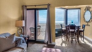 Ein Zimmer mit einer Couch, einem Tisch mit Stühlen, einer Lampe und Meerblick durch große Fenster.