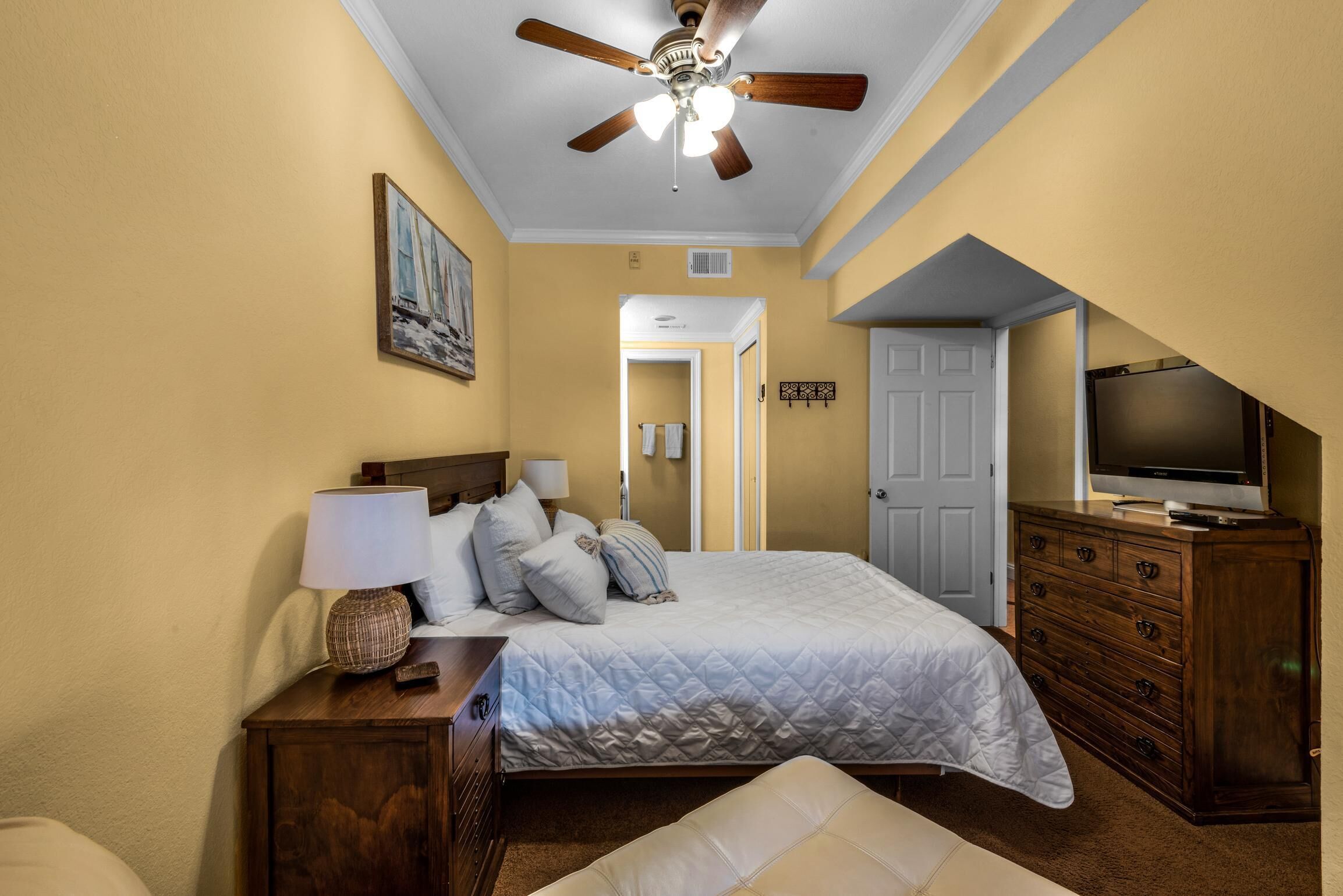 A bedroom with a bed, a nightstand, a dresser, a television, and a ceiling fan.