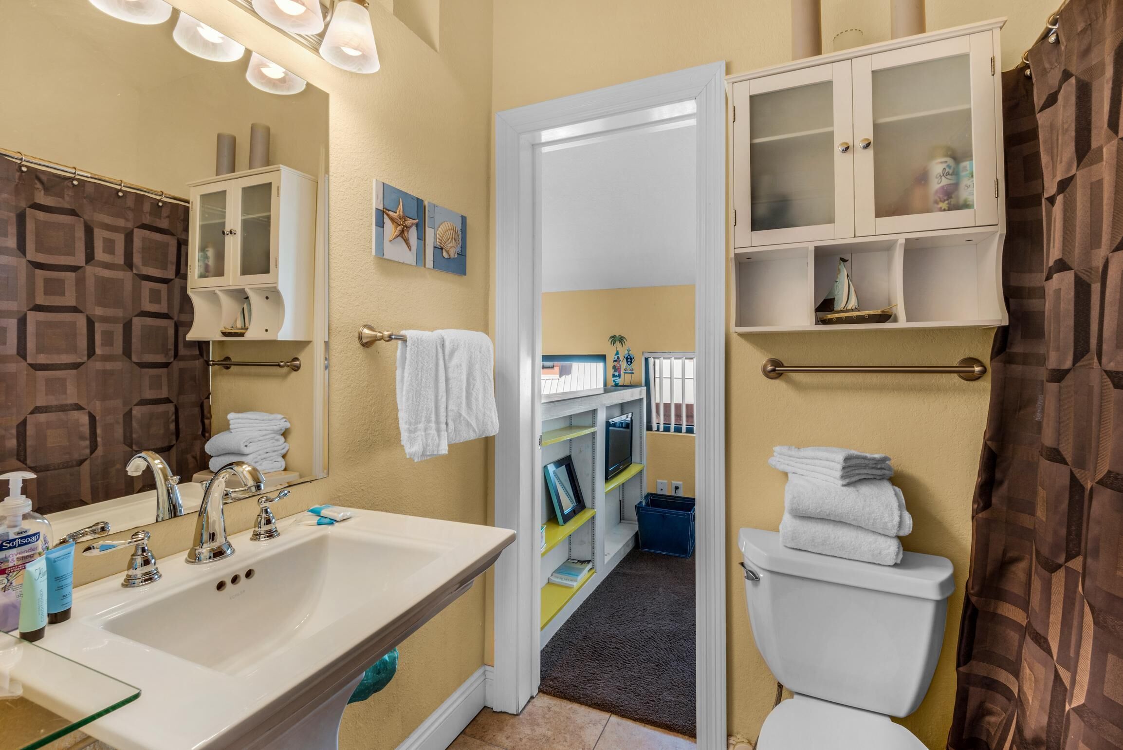 A bathroom with a white sink, a mirror, a toilet, and a cabinet with glass doors.