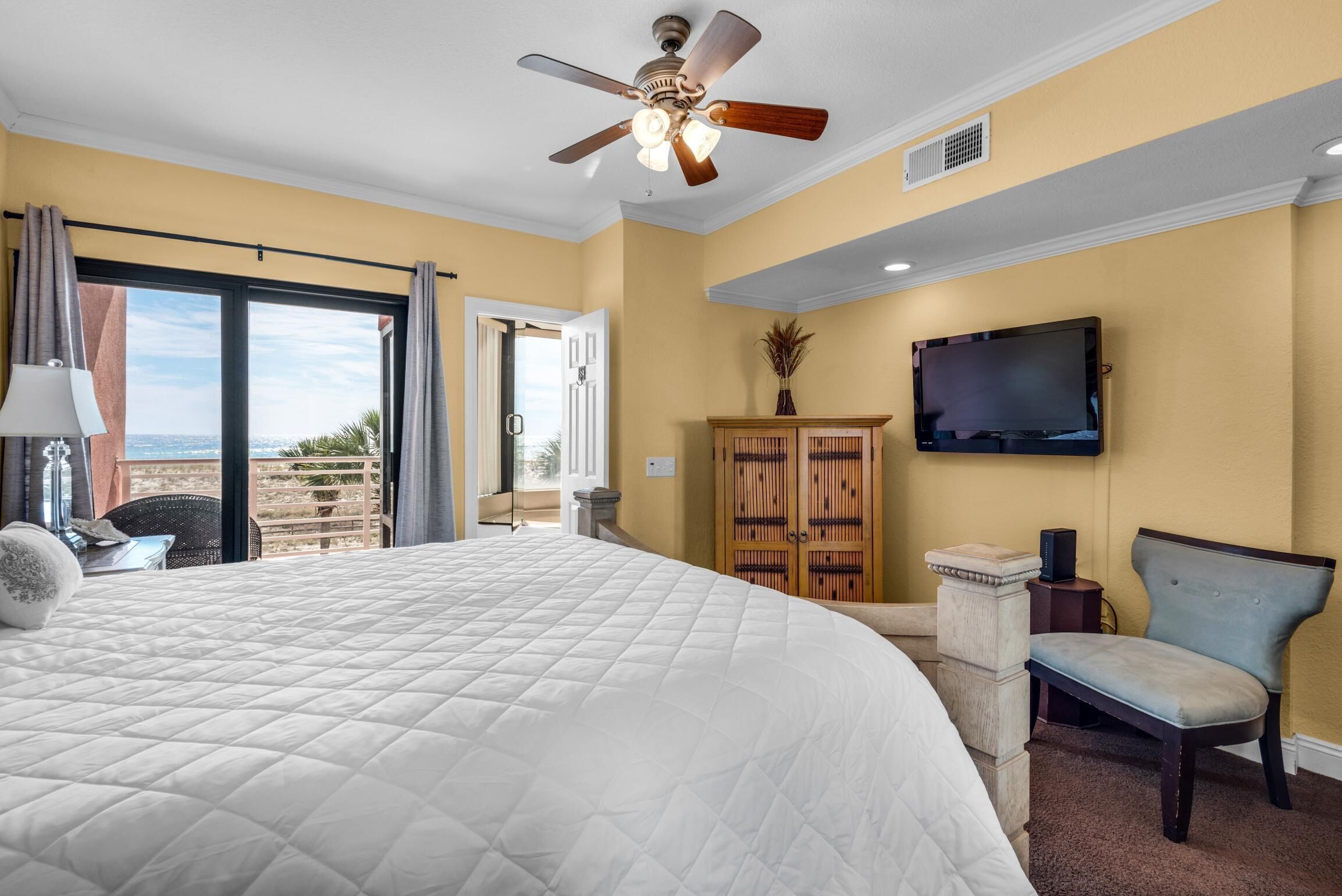 Habitación de hotel con una cama grande, ventilador de techo, televisor y vistas al exterior.