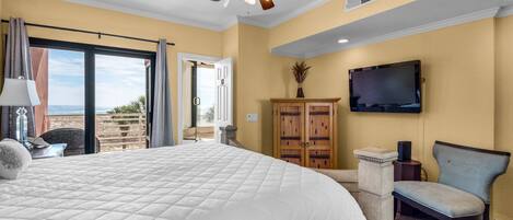 Habitación de hotel con una cama grande, ventilador de techo, televisor y vistas al exterior.
