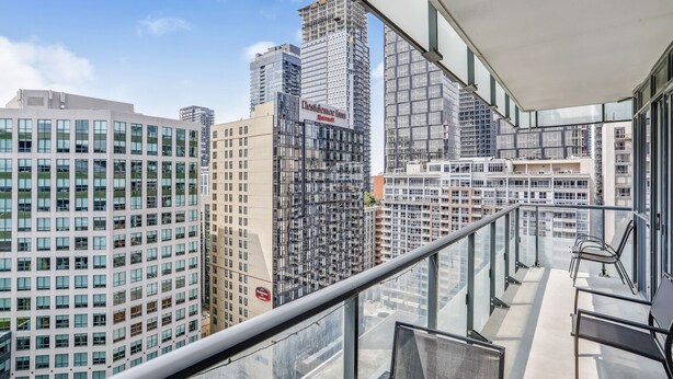 A high-rise building with a glass facade, multiple balconies, and a view of other buildings.