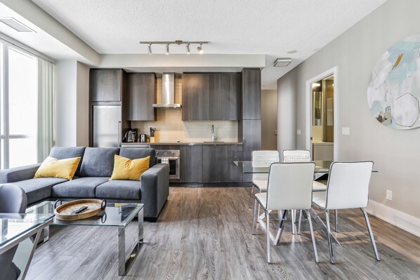 Un salon moderne avec un canapé gris, une table basse en verre et un coin repas avec des chaises blanches.