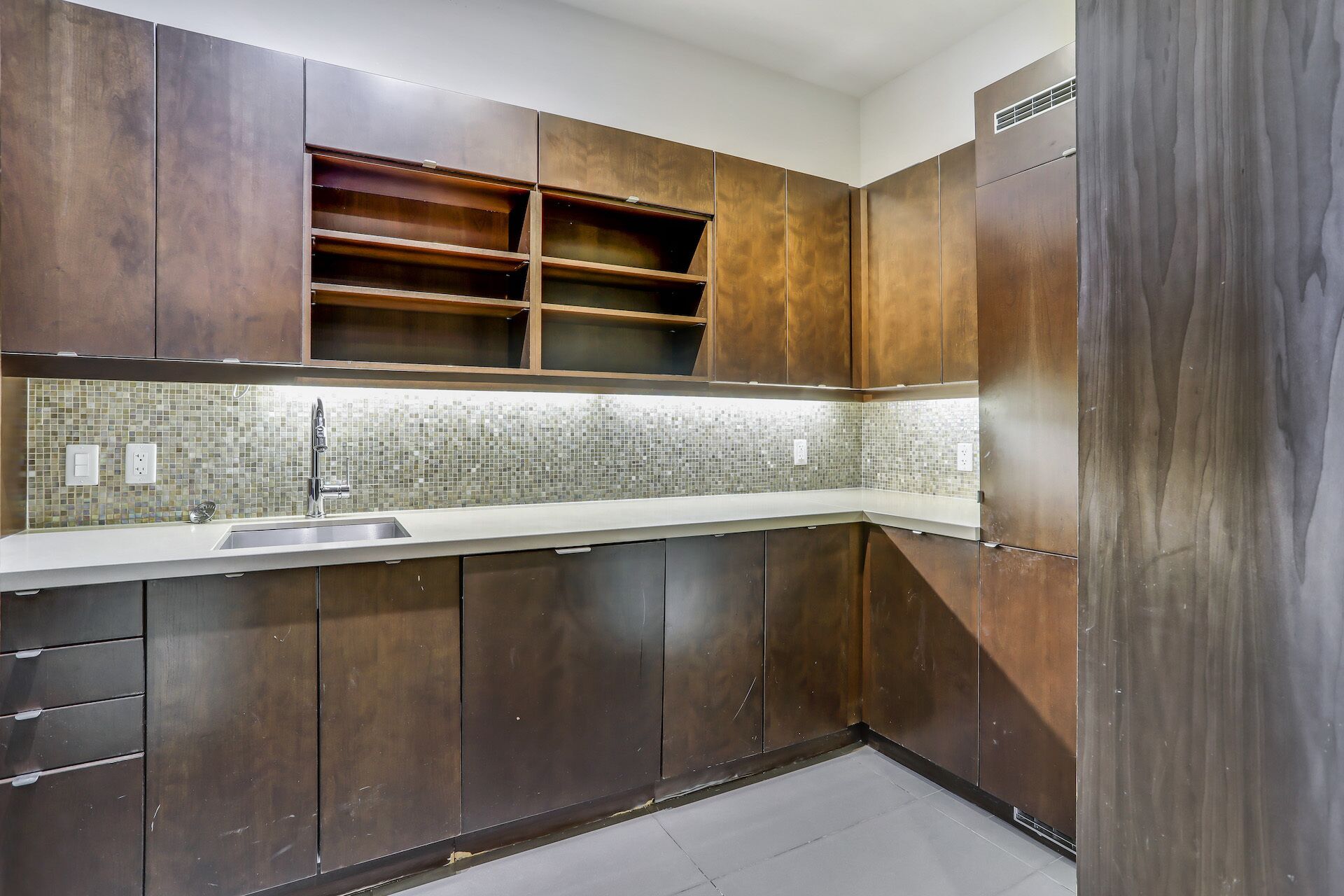 Cozinha moderna com armários de madeira escura, painel de azulejos e uma pia de aço inoxidável.